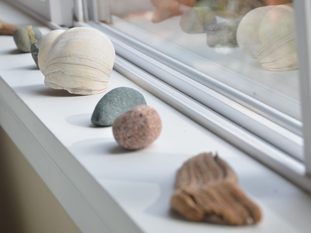 Beach stones and a shell lined up along a windowsill.