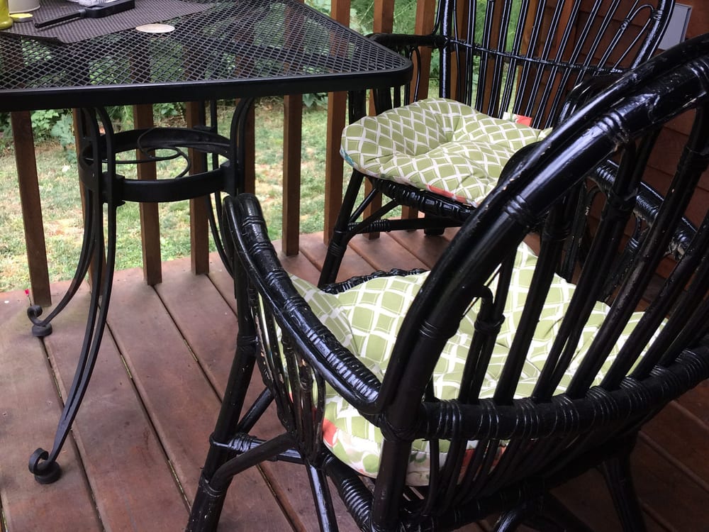 A covered balcony with a bistro table and two wicker chairs, looking out over the green farm.